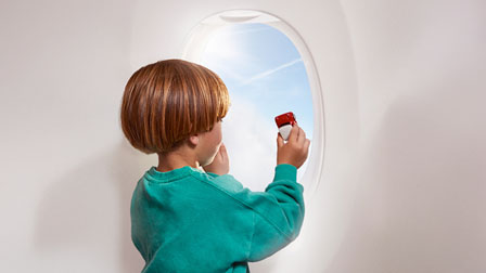 Mneores, Niños y Bebés Niño jugando en la ventana de un avión con un juguete en la mano.