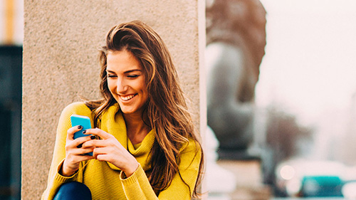 Girl looking at her phone and laughing while checking a discount code to fly with Iberia