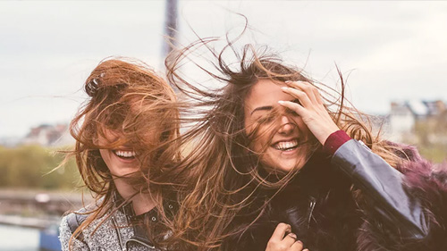 Two young women laughing as the wind blows their hair 