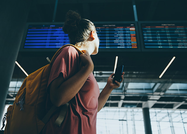  Girl with her mobile phone looking at the flight information screens at the airport