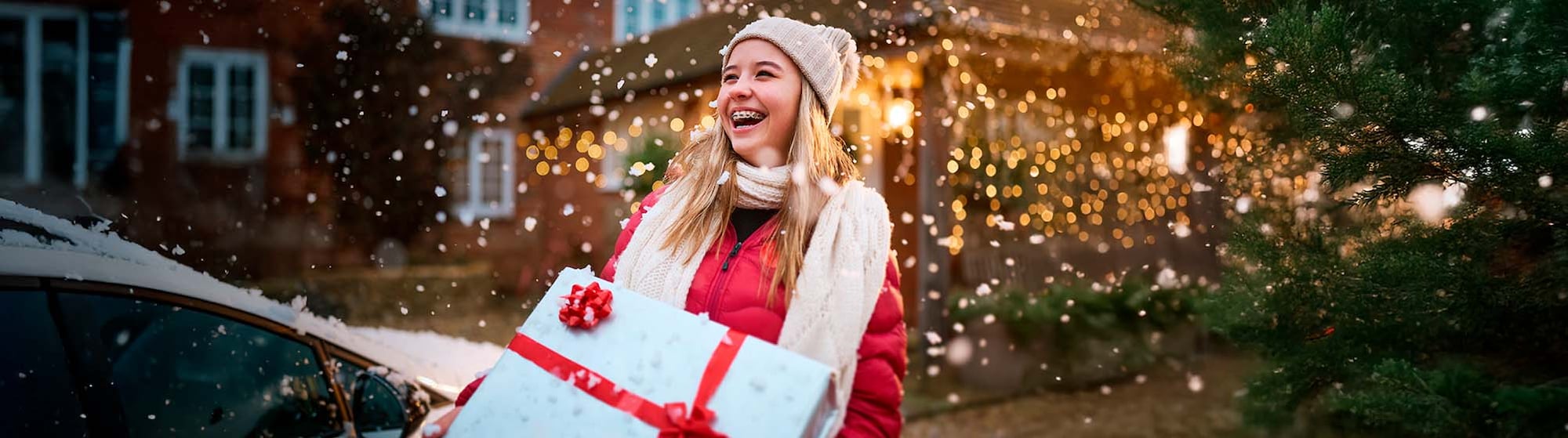 The image shows a smiling girl holding a gift in her hands.