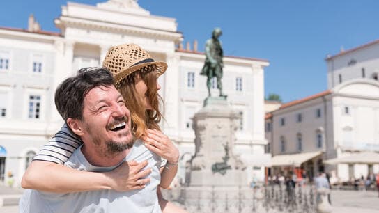 The image show a couple enjoys a happy moment together in front of a monument on a sunny day.