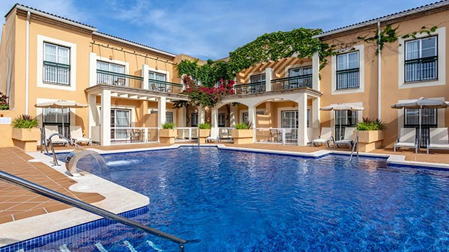 Vista de la piscina de l'Hotel Zafiro Menorca, envoltada de jardins tropicals i amb accés directe a la platja.