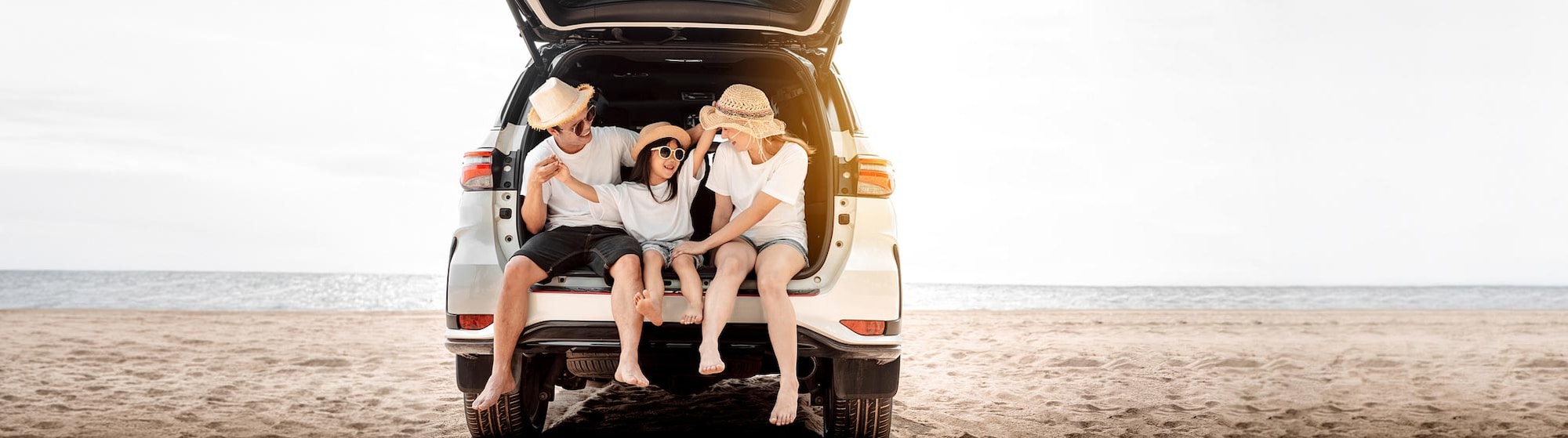 The image shows a smiling family inside an SUV parked on the beach.