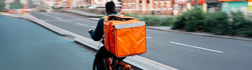 La imágen muesta una taza humeante de café en primer plano sobre la mesa, con un trozo de pastel y un croissant al fondo junto a una ventana.